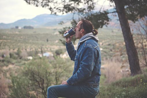 Relaxed young man drinking hot tea or coffee from a thermos mug in the early spring forest. People. Active healthy lifestyle. Leisure activity. Weekend leisure