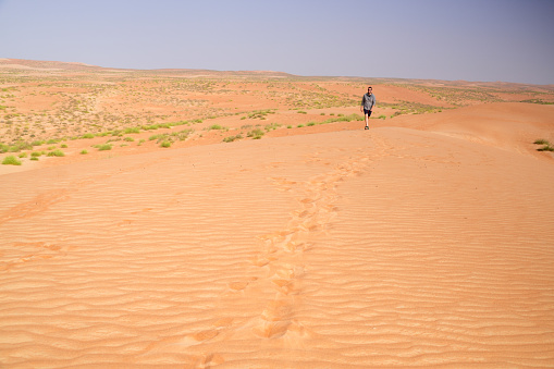 Man in short pants, walking, following the footprints on sand in Wahabi desert in Oman. In background is sand and sky.