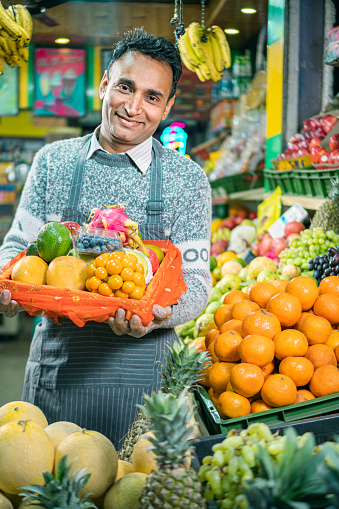 A cheerful shopkeeper sells various fresh fruits in a small store, utilizing maximum space for display.