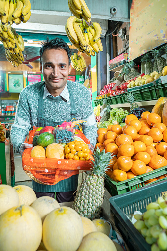 A cheerful shopkeeper sells various fresh fruits in a small store, utilizing maximum space for display.