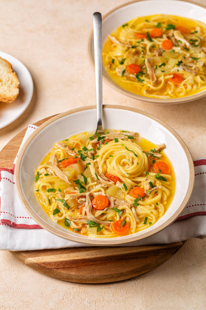 istock Chicken noodle soup in a white plate, on a wooden board. On a beige table. Vertical image. 2075241538