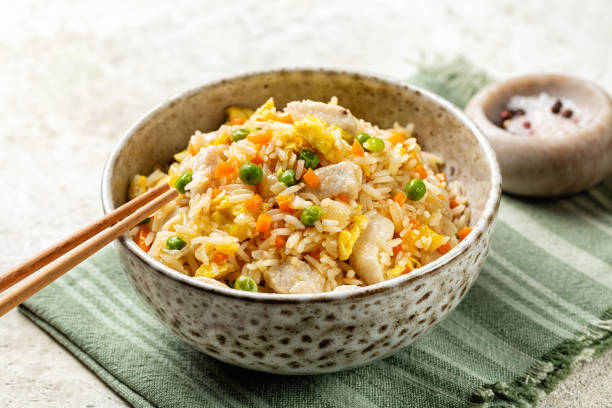istock Bowl with fried long rice, chicken, egg and vegetables, onion, bell pepper, carrot, green peas. Beige table with napkin. 2075241621