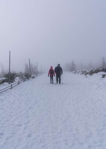 A man and a woman walk through a snowy landscape. Very poor visibility due to fog and heavy snow. View from Sniezka (Snezka) mountain in winter, Giant Mountains.Karkonosze (Krkonose)