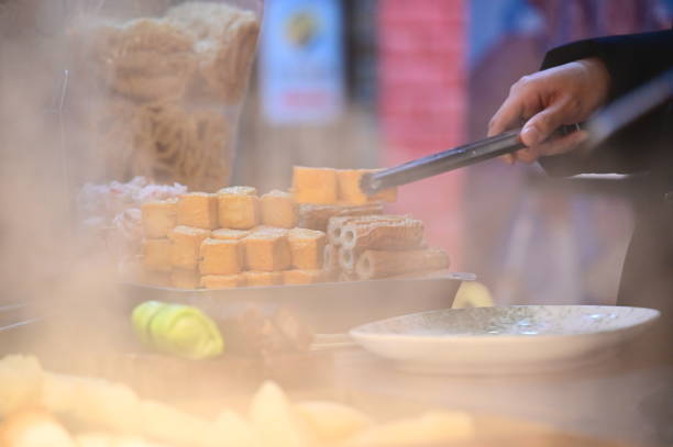 Taiwan - Jan 23, 2024: A customer is picking up a fish cake skewer from a simmering pot of oden at a night market in Taiwan. Oden is a popular and affordable snack in Taiwan.