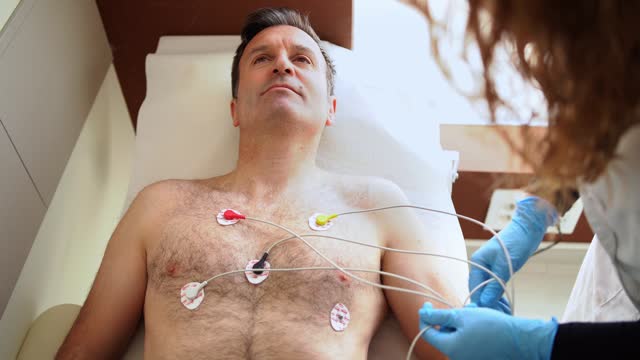 Female doctor preforming an electrocardiogram of male patient