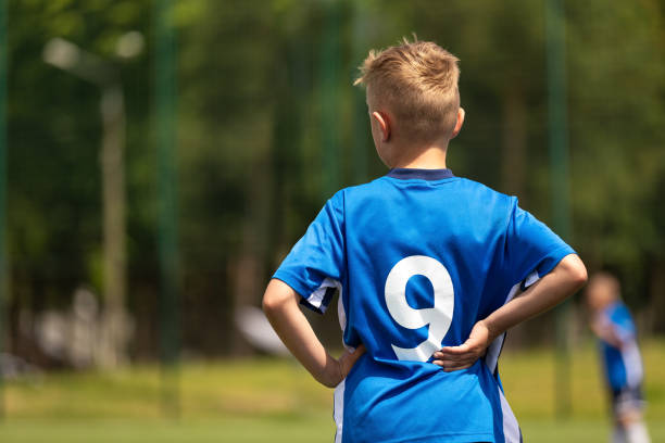 boy playing soccer with teammates. the soccer boy plays as a forward. kids soccer team in a soccer league match. a child in a blue football uniform with the number nine on back - soccer child coach childhood imagens e fotografias de stock