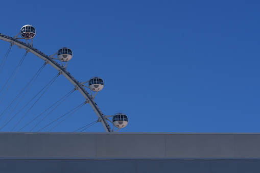 A minimalist yet striking photograph featuring the apex of a Ferris wheel against a clear blue sky. The image emphasizes the geometric beauty and engineering marvel of the wheel's design, with its sleek capsules poised high above the ground, offering riders a glimpse of the city from the heavens. The stark contrast between the man-made structure and the vastness of the sky invites contemplation of the human desire to rise above and see the world from a new perspective.
