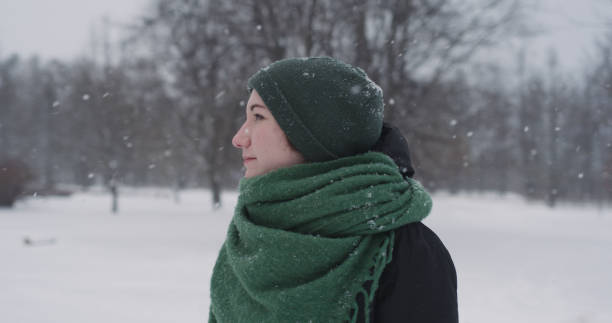 istock girl standing in park on winter day under snowfall 2075335744