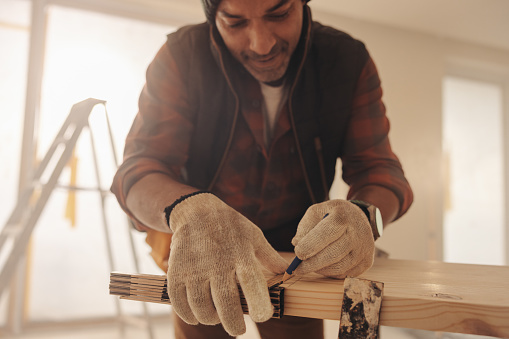 Contractor measuring and marking a plank for a kitchen renovation. With expertise, he works on the baseboards and carpentry, upgrading the home interior with skilled woodwork and craftsmanship.