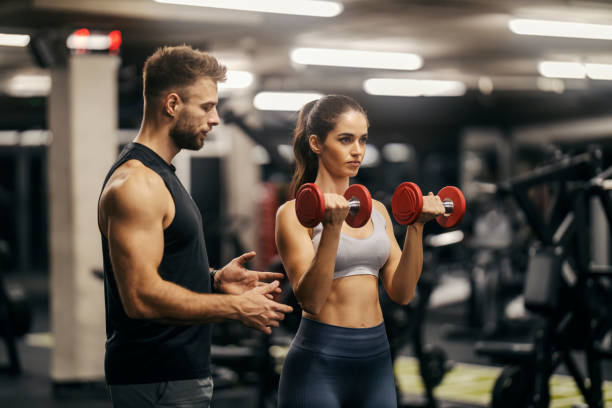 istock A fit sportswoman is doing biceps curls in a gym while her trainer is encouraging her. 2075353092