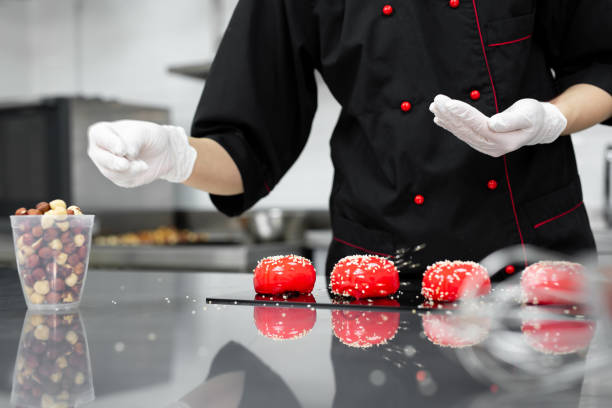 The pastry chef sprinkles the red mousse cake with sesame seeds.