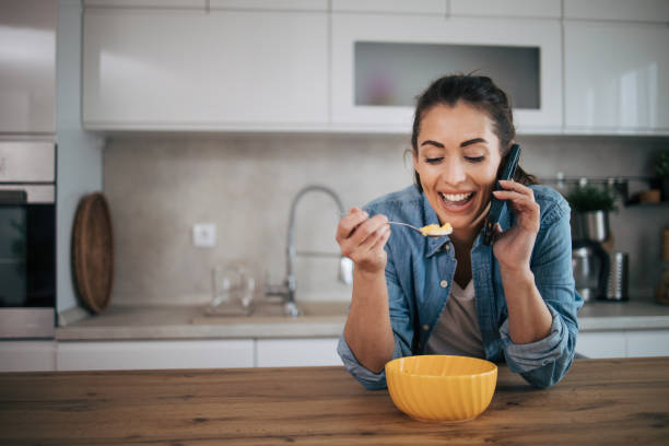 istock Young woman using the mobile phone while eating cereal with milk 2075378853