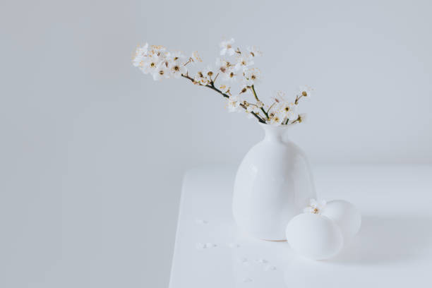 Beautiful blossom branches in a vase and eggs on a white background. Spring minimalistic concept. Place for text.
