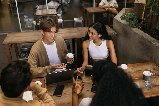 Group of multiracial college students communicating while studying over computers in a café.