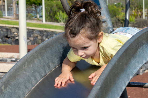 The child has fun rolls from the slide on the site. A happy little girl, first gliding along a slide on a bright red playground, enjoying a warm sunny day, enjoying carefree moments in the park..