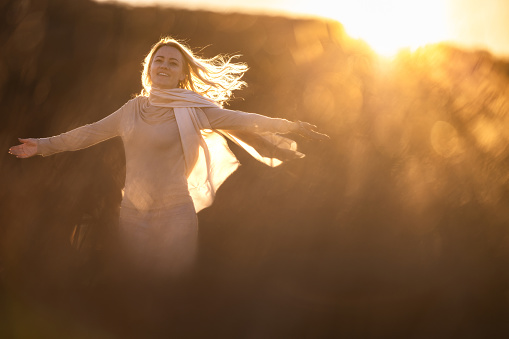 Happy woman raising her hands in nature during sunset
