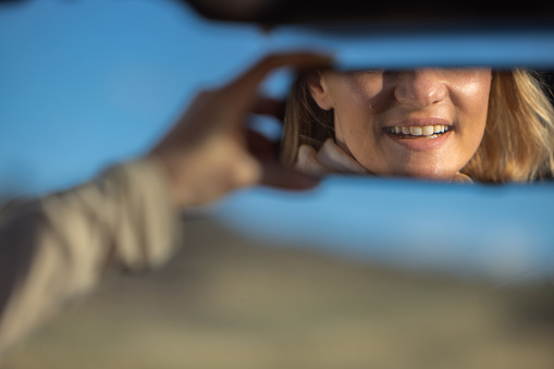 Close-up of reflection of a woman with a smile on the car mirror