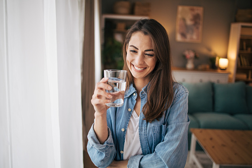 Young woman drinking glass of water standing at home