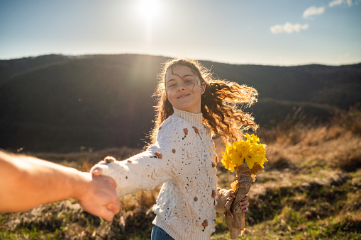 Happy teenage girl whit curly hair with bouquet of flowers holding hand of unknown person in nature