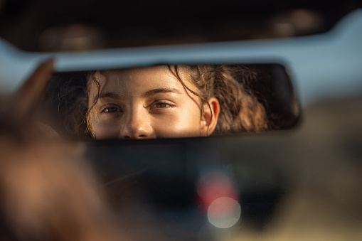 Happy teenage girl looking in car rear view mirror