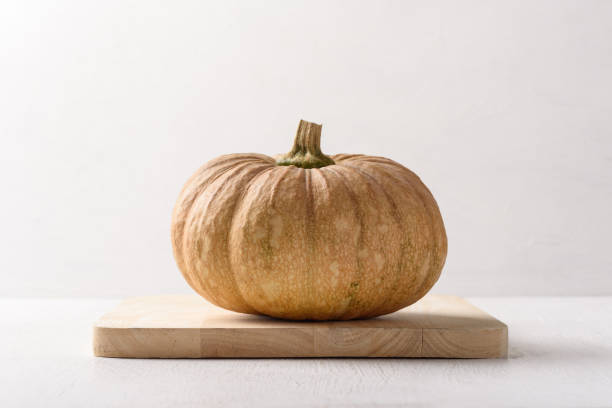 Local pumpkins are placed on a light brown wooden plank on a white background. Organic ingredients for healthy cooking stock photo