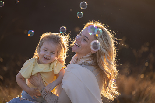 Happy single mother and her little daughter are spinning in nature surrounded by bubbles