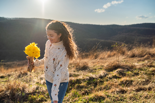 A happy teenage girl is carrying a bouquet of flowers while walking on a mountain during a sunny day