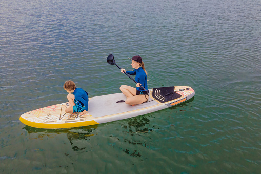 Mother and son paddling on stand up board having fun during summer beach vacation.