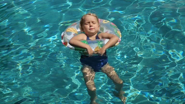 Girl with closed eyes lounges in pool on inflatable ring. Cinematic video of happy kid spend summer vacation on inflatable ring on pool. Concept: enjoy moments of poolside calm with inflatable ring.