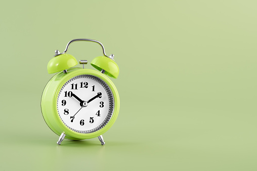 Green vintage alarm clock on a pastel green background, depicting the concept of time management or morning routine.