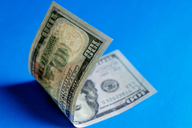 One hundred US dollars  bill in close-up casting shadows , folded in half on a blue background