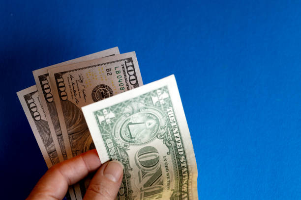 Financial concept. One dollar and a hundred dollars in a woman's hand on a blue background