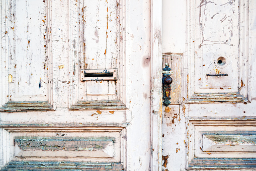 Old wooden door. White weathered paint is flaking and peeling of the surface. Grungy texture and background.