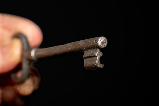 A close-up shot of a hand holding a silver key against a black background