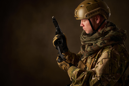 portrait of an airsoft soldier in camouflage clothing reloading airsoft pistol