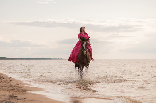 A woman gracefully rides a horse in the water on the beach
