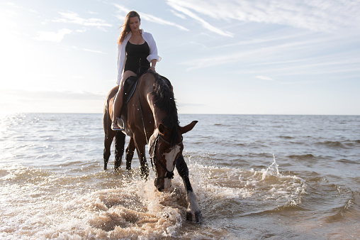 A woman on horseback emerges from the ocean on a beach