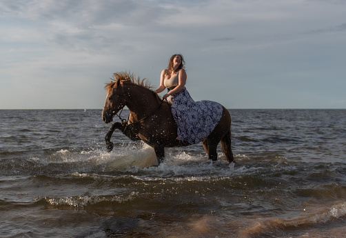 Woman in a flowing dress rides horse in water