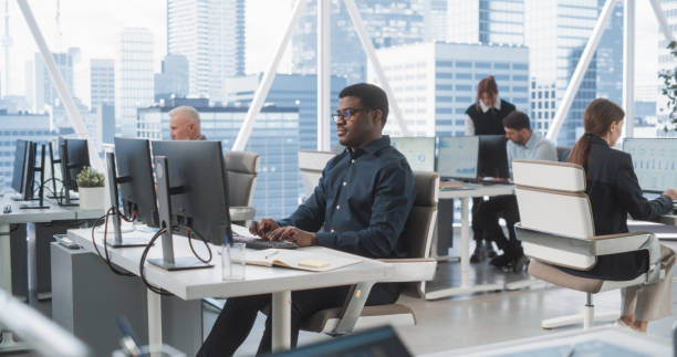 istock Focused African American Male Data Analyst Typing On Desktop Computer In Diverse Corporate Office With Megapolis Window View. Professional Balck Man Working In Consulting Company With Colleagues. 2075454589