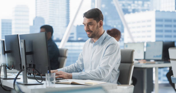 istock Happy Male Sales Manager Typing On Desktop Computer In Diverse Corporate Office With Megapolis Window View. Proffesional Caucasian Man Smiling After Closing Big Advertising Deal For E-commerce Company 2075454665