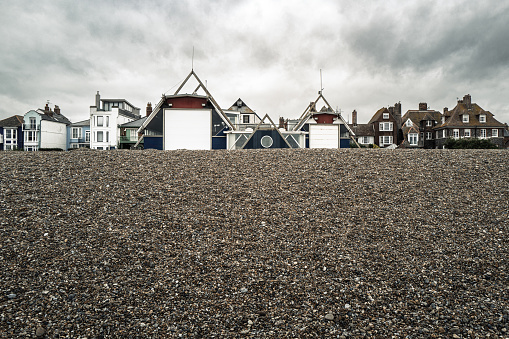 Near ground level view of a stony beach of the Suffolk coast. The distance shows both costal holiday lets and houses together with a lifeboat station.