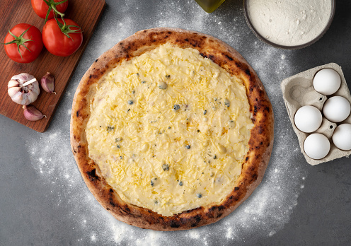 Four cheese pizza with tomatoes, eggs and flour over stone background.