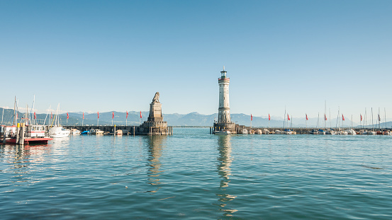 Lindau, Germany - August 02 2013: Lighthouse and lion statue at the entrance to Lindau harbor on a sunny afternoon. Other bank of the lake is visible in background. Numerous boats are moored to mole.