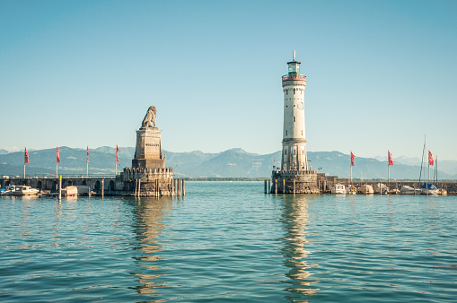 Lindau, Germany - August 02 2013: Lighthouse and lion statue at the entrance to Lindau harbor on a sunny afternoon. Other bank of the lake is visible in background. Numerous boats are moored to mole.