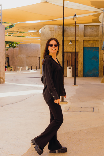 Side view of female in black casual clothes walking the old streets with authentic Persian buildings at Al Bastakya district of Dubai city, United Arab Emirates