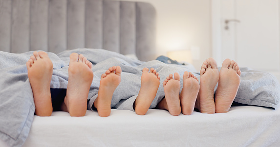 Sleeping feet, relax and family in bed with love, bond or security at home together. Barefoot, children or parents in a bedroom with comfort, trust and care, protection or nap with safety in a house