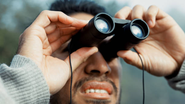 istock Face, hiking and man with binocular in nature for sightseeing, explore or trekking a mountain environment. Travel, adventure and view with a young male hiker closeup outdoor in the woods or forest 2075510194