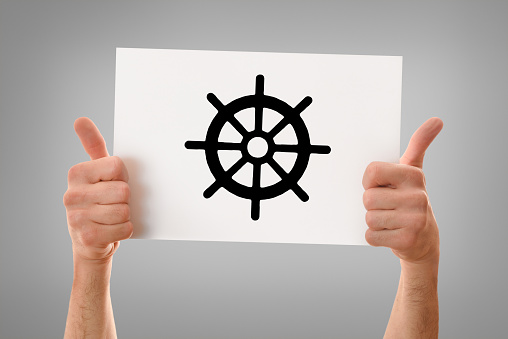 Hands of a religious man with okay sign holding a white poster drawn dharma wheel gray isolated background