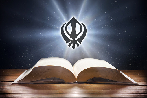 Open book on wooden table and sikh symbol with beam of light with dark background. Front view.