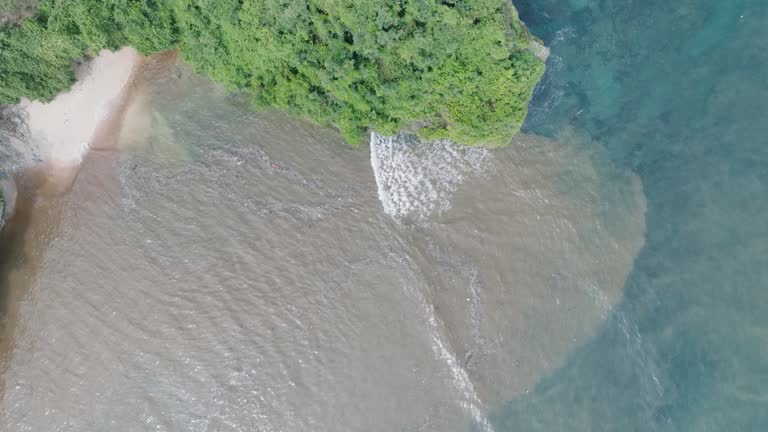 Top down aerial drone shot over polluted sewage water and floating trash with debris over dead coral reef mixing with turquoise water and tropical coastine in Bali Indonesia